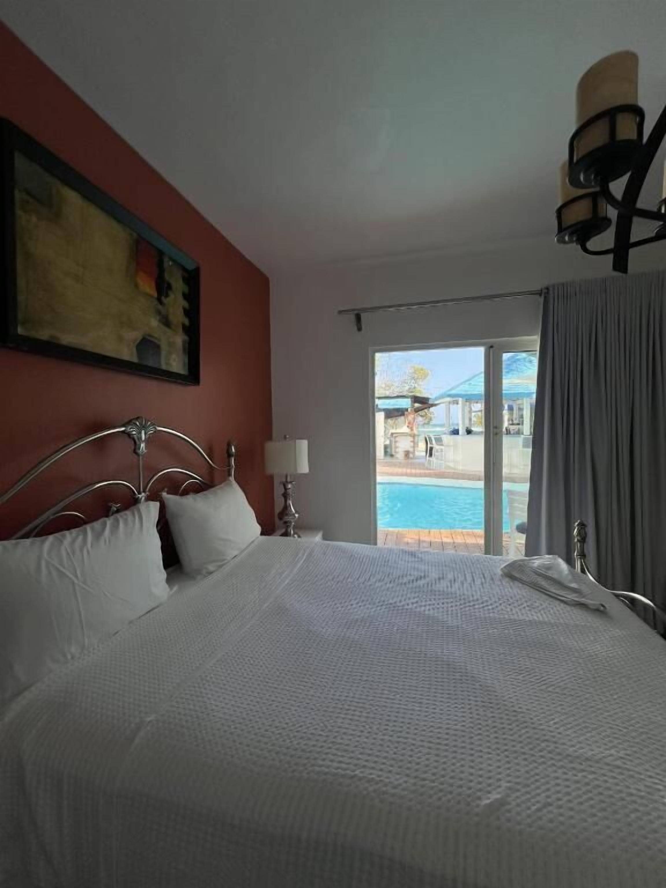 A hotel room with a bed, a painting on the wall, a lamp, and a view of a swimming pool.