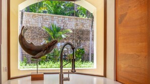 A modern kitchen with a stainless steel sink, a decorative horn sculpture, and a view of a stone wall and greenery outside. - Beachfront Villa, Ocean Views, Resort Pools, Steps to Playa Flamingo (Playa Flamingo)