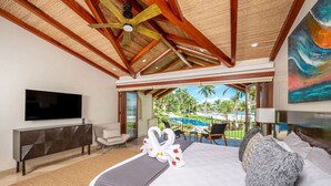 A hotel room with a large bed, a flat-screen TV, a seating area with chairs, and a view of a pool and palm trees. - Beachfront Villa, Ocean Views, Resort Pools, Steps to Playa Flamingo (Playa Flamingo)