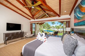 Ein Hotelzimmer mit einem großen Bett, einem Flachbildfernseher, einer Sitzecke mit Stühlen und Blick auf Pool und Palmen.
