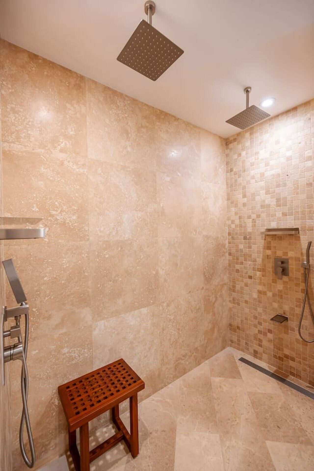 A shower area with a square showerhead, a handheld showerhead, and a small wooden stool.