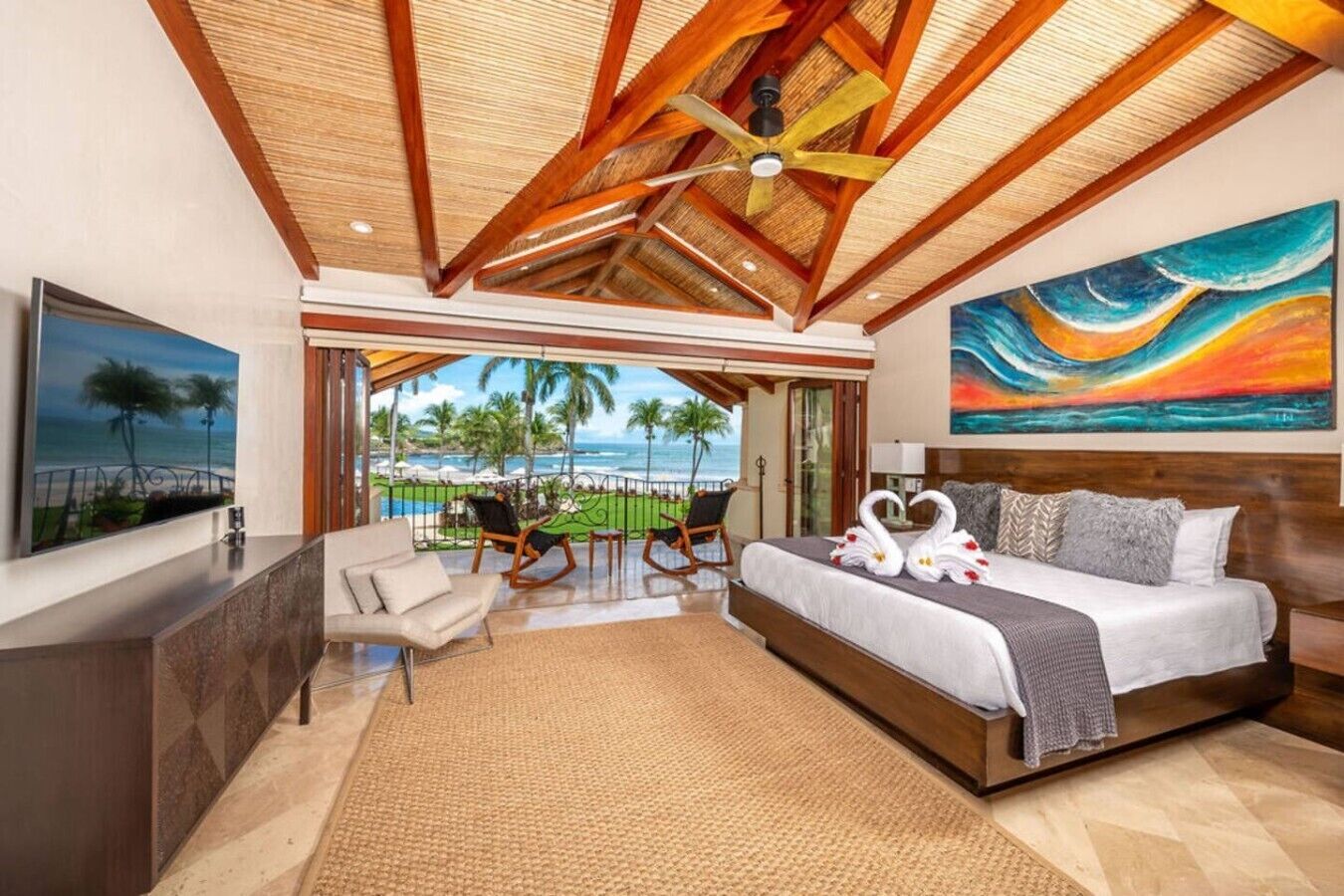 Habitación de hotel con cama, vista al océano, un cuadro y balcón con sillas.