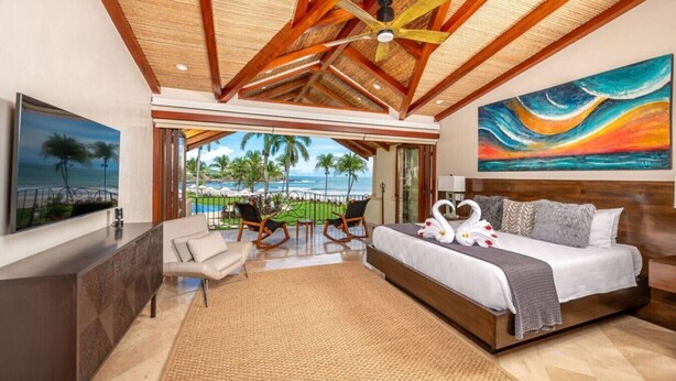 A hotel room with a bed, a view of the ocean, a painting, and a balcony with chairs. - Beachfront Villa, Ocean Views, Resort Pools, Steps to Playa Flamingo (Playa Flamingo)