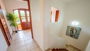 Un couloir avec une porte en bois, une plante en pot et un tableau accroché au mur.