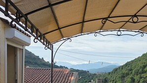 A covered outdoor seating area with a table and chairs, overlooking a mountainous landscape. - Village house (Castifao)