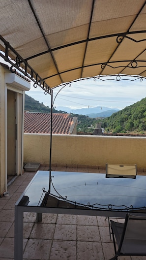 Ein überdachter Außenbereich mit Tisch und Stühlen, mit Blick auf eine gebirgige Landschaft.