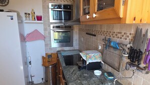 A kitchen with wooden cabinets, a stainless steel sink, a microwave, and an oven. - Village house (Castifao)