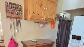 A kitchen with wooden cabinets, a hanging spice rack, a refrigerator, and a dining area with a chair. - Village house (Castifao)
