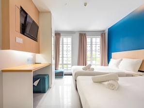 Habitación de hotel con cama, escritorio, televisor y ventana con cortinas.
