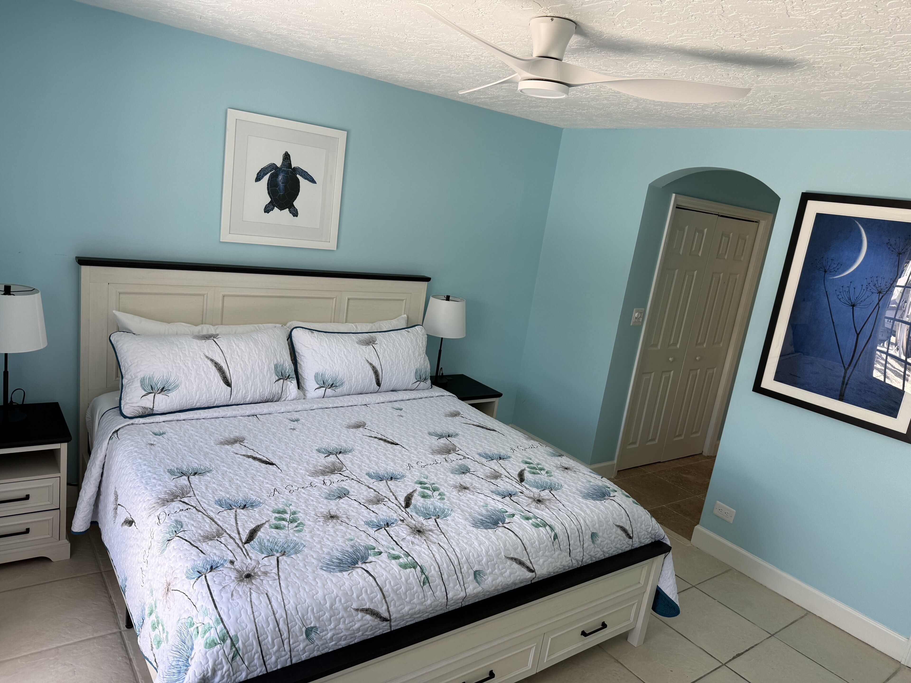 Una camera da letto con un letto, comodini, una ventola a soffitto e opere d'arte alle pareti.