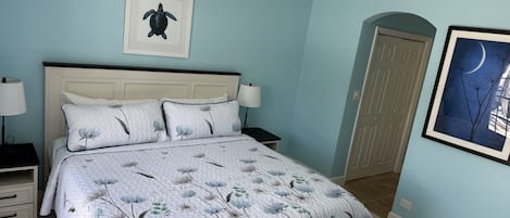 Un dormitorio con cama, mesitas de noche, ventilador de techo y obras de arte en las paredes.