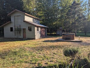 A two-story wooden cabin with a garage, a small shed, and a hot tub in a grassy area with trees. - Park like setting on the Applegate River great for wine tasting & family reunion (Jacksonville)
