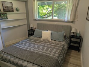 A bedroom with a bed, two nightstands, a window with curtains, and a shelf with books and a globe. - Park like setting on the Applegate River great for wine tasting & family reunion (Jacksonville)