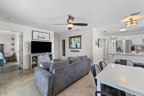 A modern living room with a gray sofa, a flat-screen TV, and a ceiling fan.