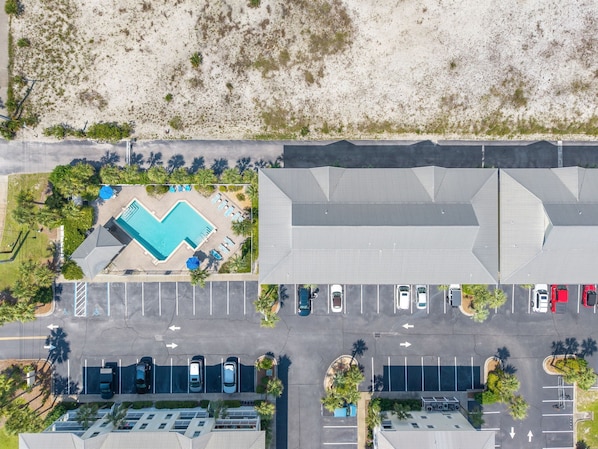 An aerial view of a hotel with a swimming pool, parking lot, and adjacent beach.