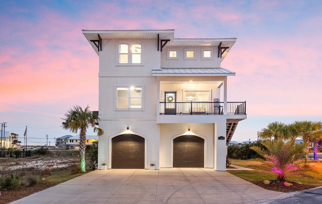 A two-story house with a balcony, two garage doors, and a well-lit driveway.
