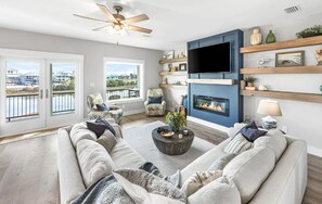 Een woonkamer met een open haard, een televisie aan een blauwe muur en een balkon met uitzicht op het water.