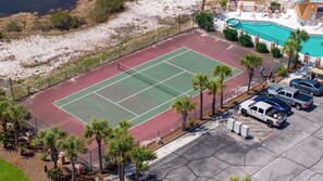 An aerial view of a tennis court surrounded by palm trees, adjacent to a swimming pool and a parking area with several vehicles. - 🐾 Sound & Sea | Pet Friendly Gated Community | Bikes + Beach Gear Navarre (Navarre)