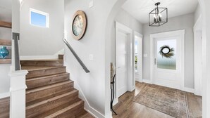 A staircase with wooden steps and white railings, a wall clock, a door with a wreath, and a chandelier. - 🐾 Sound & Sea | Pet Friendly Gated Community | Bikes + Beach Gear Navarre (Navarre)