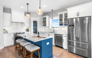 A modern kitchen with white cabinets, a stainless steel refrigerator, a blue island with bar stools, and pendant lighting. - 🐾 Sound & Sea | Pet Friendly Gated Community | Bikes + Beach Gear Navarre (Navarre)