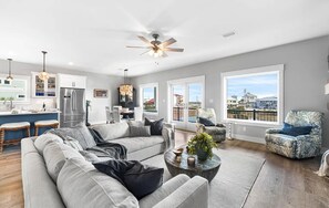 A spacious living room with a gray sectional sofa, a coffee table, and a view of the city through large windows. - 🐾 Sound & Sea | Pet Friendly Gated Community | Bikes + Beach Gear Navarre (Navarre)