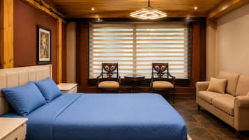 Ein Hotelzimmer mit Bett, einer Couch, zwei Sesseln, einem kleinen Tisch und einem Fenster mit Jalousien.