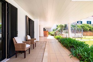 A covered outdoor area with wicker chairs, a tiled floor, and a garden with green plants. - SunDream Apart I (Funchal)