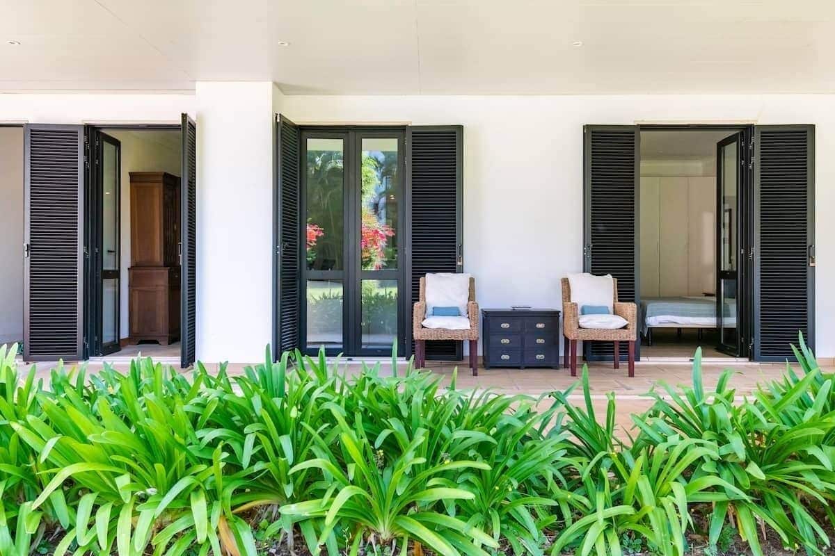 A covered outdoor seating area with two chairs and a small table, flanked by open doors leading to interior spaces.