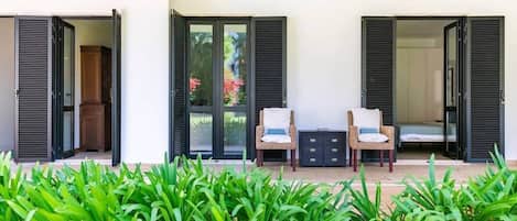 A covered outdoor seating area with two chairs and a small table, flanked by open doors leading to interior spaces.