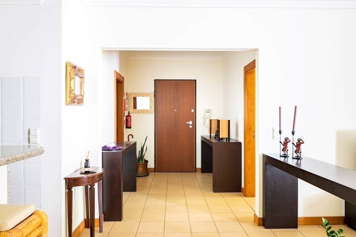 A hotel lobby with a reception desk, a wooden door, a small table with a plant, and a wall-mounted mirror.
