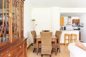 A dining area with a wooden cabinet, wicker chairs, and a kitchen in the background. - SunDream Apart I (Funchal)
