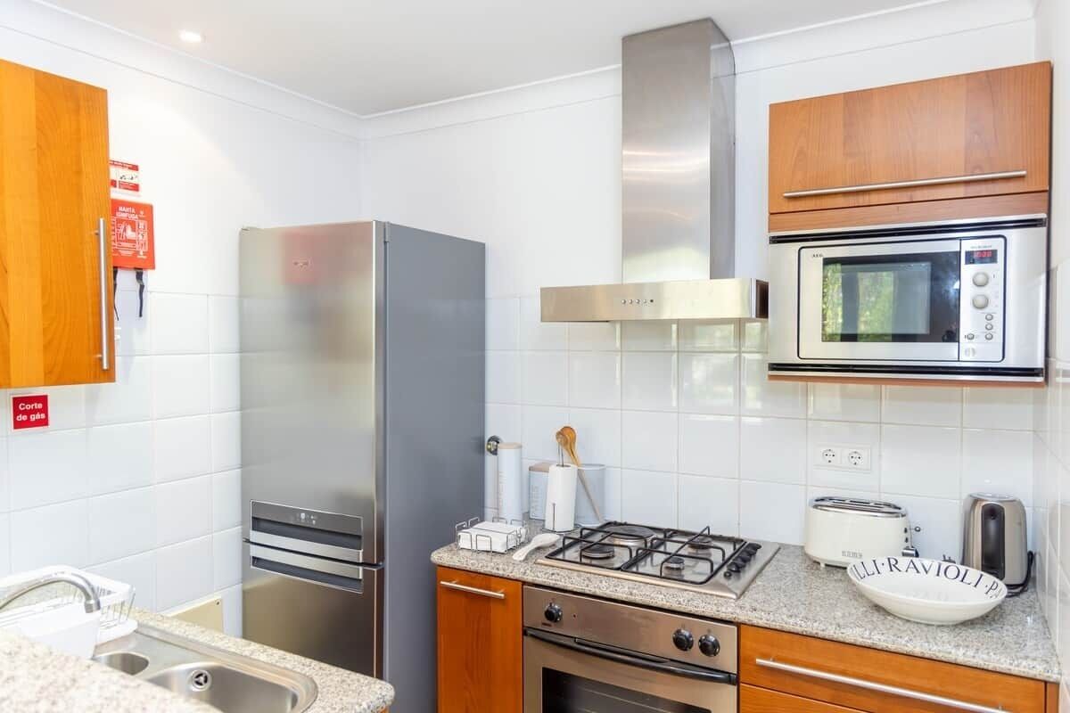 Una cocina moderna con electrodomésticos de acero inoxidable, estufa a gas, microondas y armarios de madera.