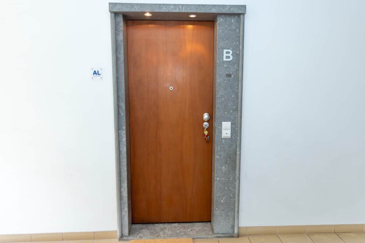 A wooden door with a metal handle and a keyhole, marked with a letter 'B' on the wall beside it.