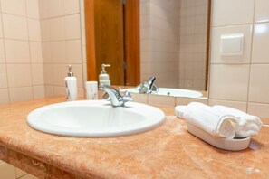 Ein Badezimmer mit weißem Waschbecken, einem Spiegel, einem Handtuchhalter und Pflegeprodukten.