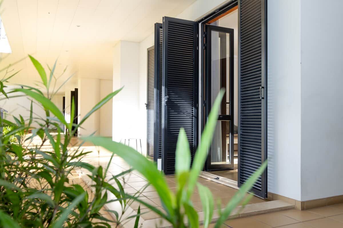 A hallway with a door leading to a room, a tiled floor, and a plant in the foreground.