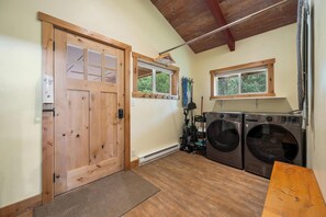 Una sala de bugaderia amb dues rentadores, una porta de fusta i una finestra que donava a arbres.