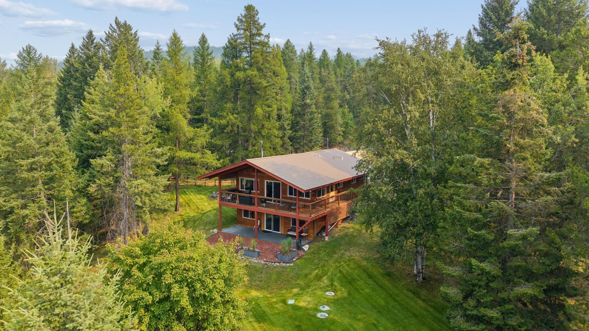 Eine zweistöckige Holzblockhütte mit einer Terrasse, umgeben von einem Wald.