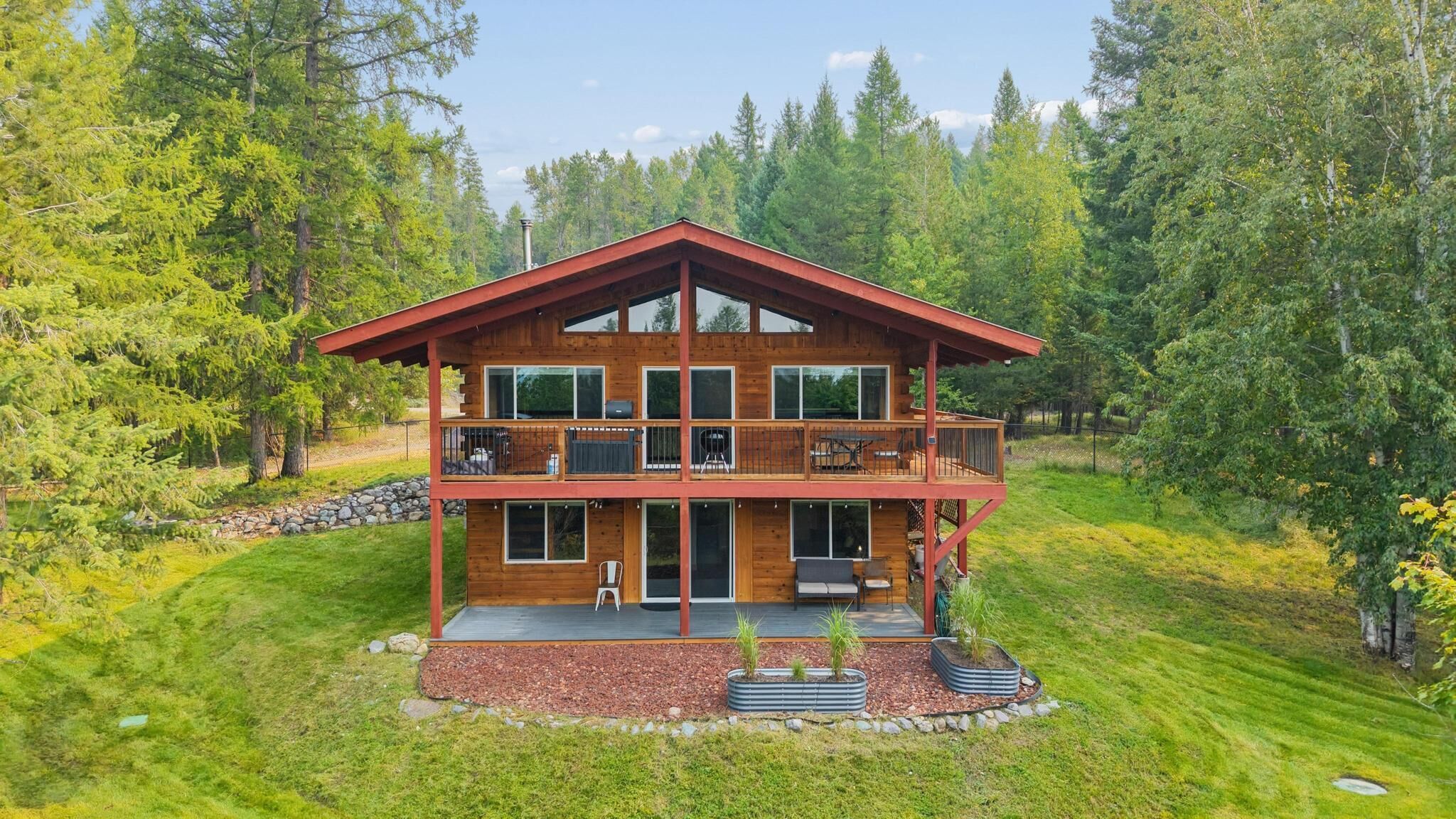 Eine zweigeschossige Holzdiele mit einem Balkon, umgeben von einem Wald.