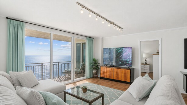 A spacious living room with a large TV, comfortable seating, a coffee table, and a view of the sea. - Oceanfront 3BR Balcony Indoor Outdoor Pools (Daytona Beach Shores)