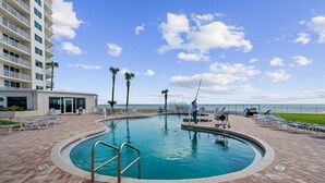 A swimming pool with a poolside area, lounge chairs, and a building with balconies in the background. - Oceanfront 3BR Balcony Indoor Outdoor Pools (Daytona Beach Shores)