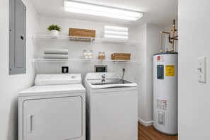 Ein Waschraum mit zwei Waschmaschinen, einem Stapel-Waschtrockner und einem Warmwasserbereiter.