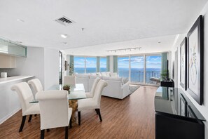 Una sala de estar moderna con vistas al océano, un comedor con mesa de vidrio y una cocina con encimera blanca.