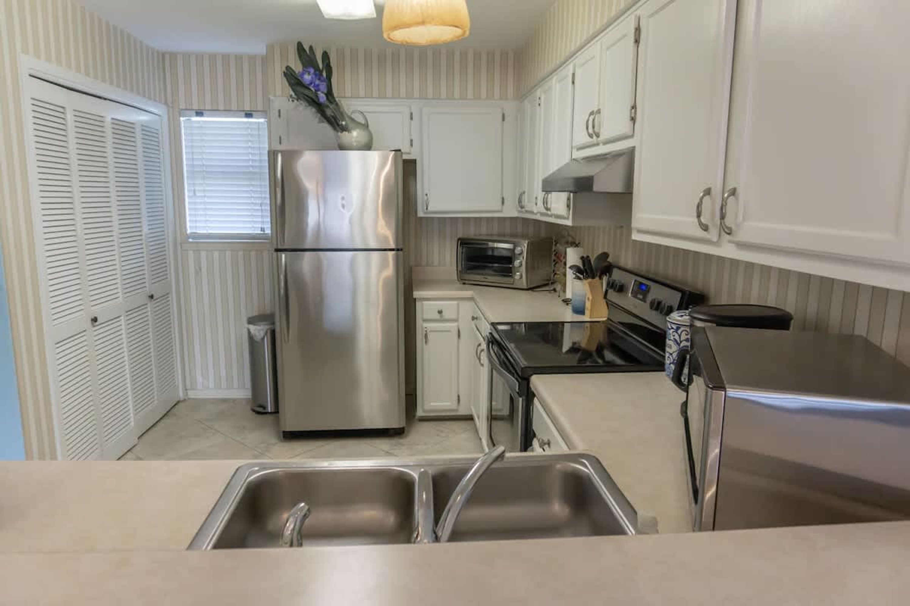 A kitchen with stainless steel appliances, a sink, and white cabinetry.