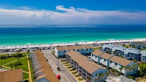A coastal hotel with multiple-story buildings, a parking lot, and a beach in the background. - Beachfront Villa With Sea Views Bikes Included Gulf Across St Kayak Access (Miramar Beach)