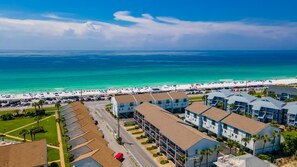 A coastal hotel with multiple-story buildings, a parking lot, and a beach in the background. - Beachfront Villa With Sea Views Bikes Included Gulf Across St Kayak Access (Miramar Beach)