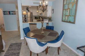 A dining area with a round table, blue and white chairs, a chandelier, and a kitchen in the background. - Beachfront Villa With Sea Views Bikes Included Gulf Across St Kayak Access (Miramar Beach)