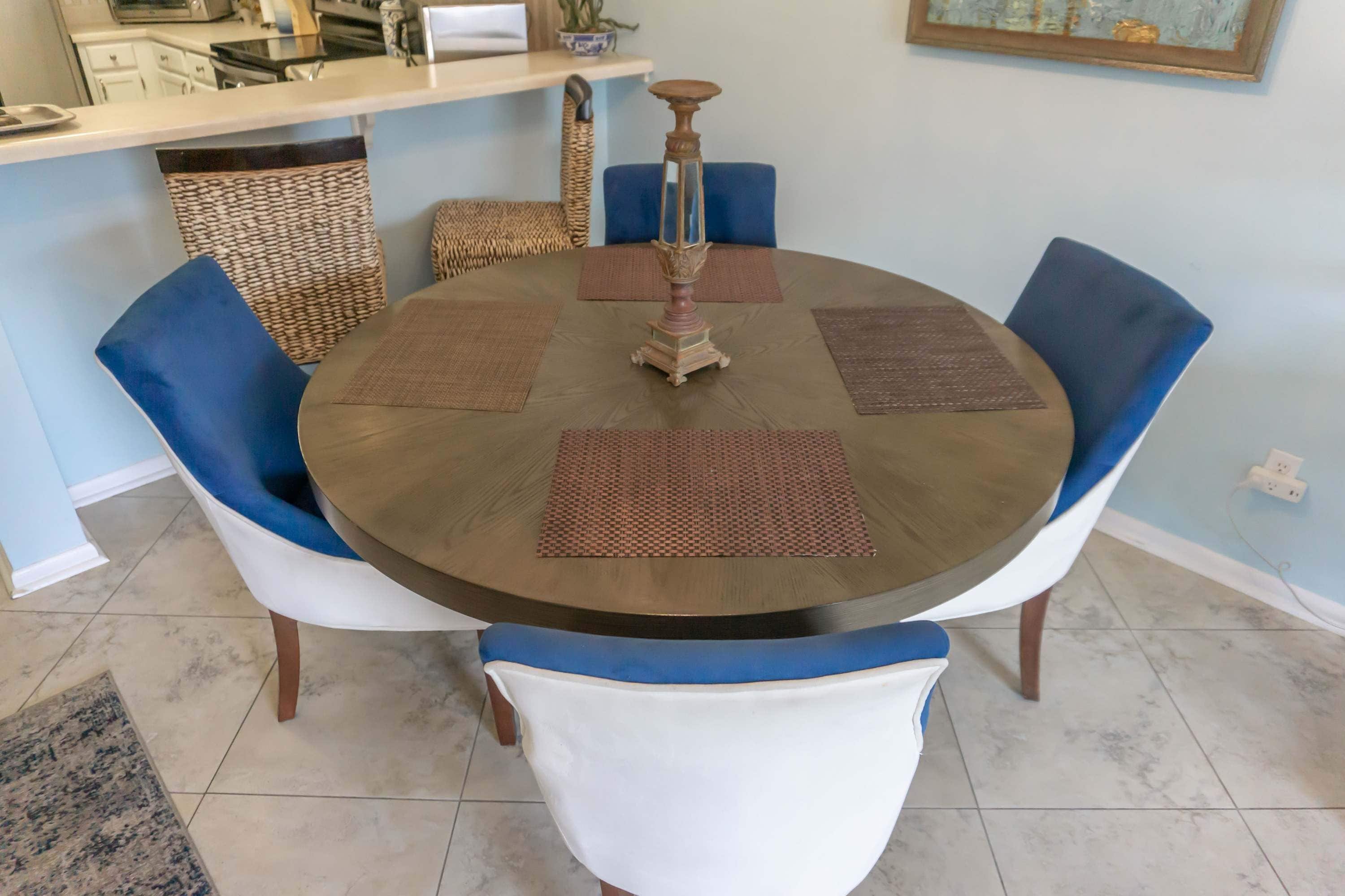 Une table de salle à manger ronde, ornée d’un chandelier central, entourée de six chaises à l’assise bleue et blanche.
