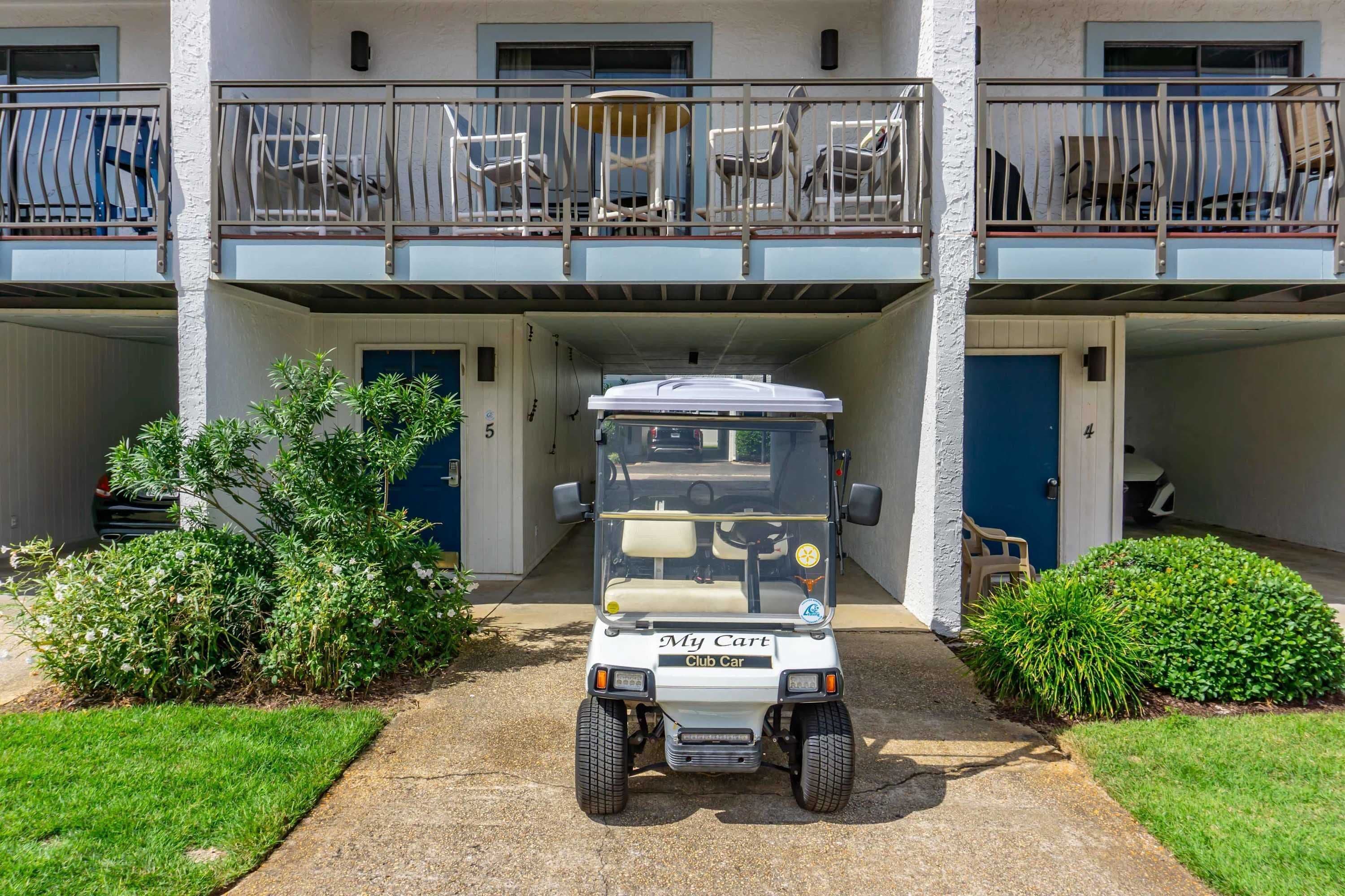 A golf cart parked in front of a building with a covered entrance and a balcony with chairs.