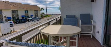 Un balcón con una mesa y dos sillas, con vistas a una calle con coches aparcados y edificios.