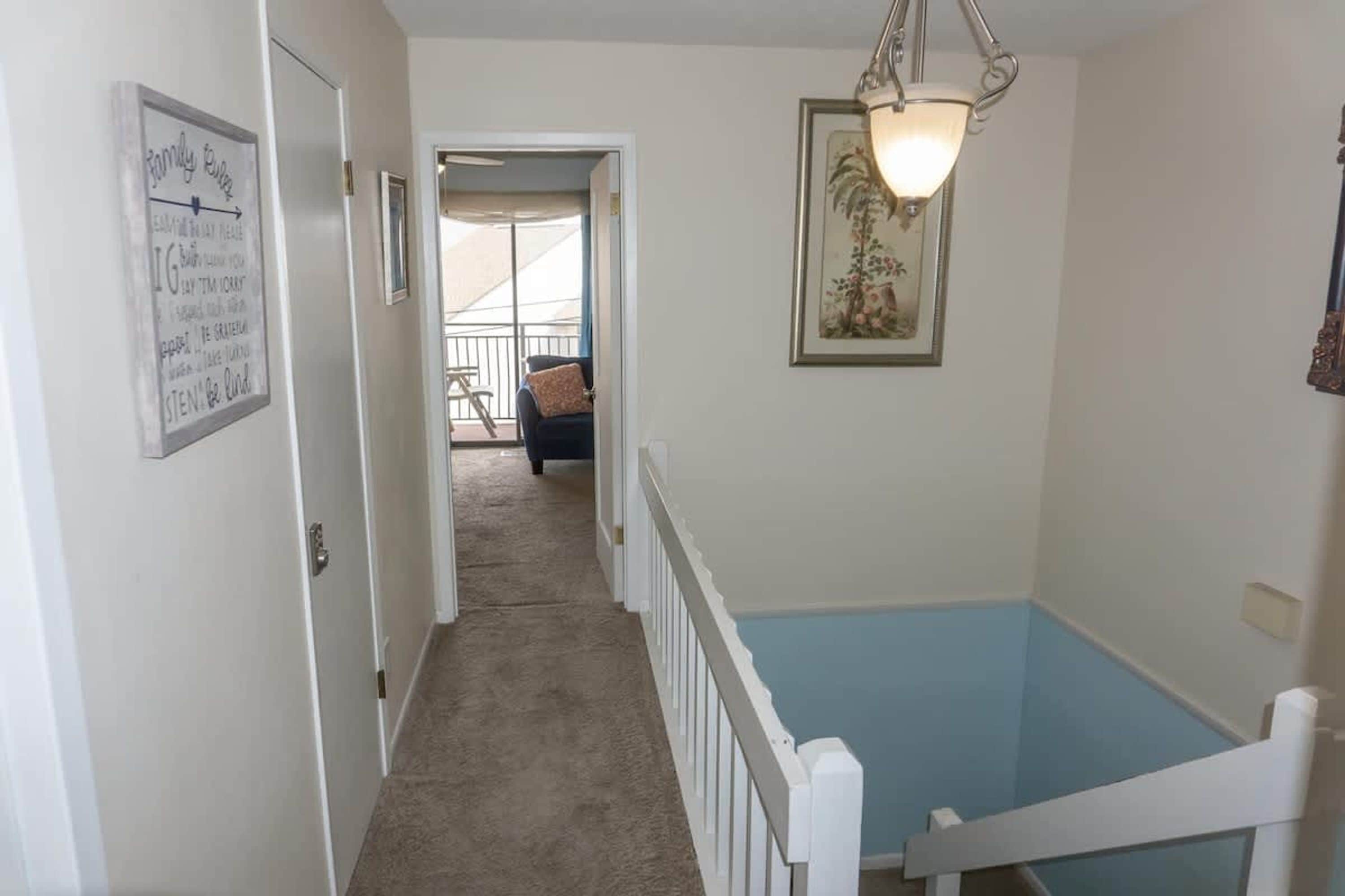 A hallway with a white railing, a door, and a staircase leading to a balcony.